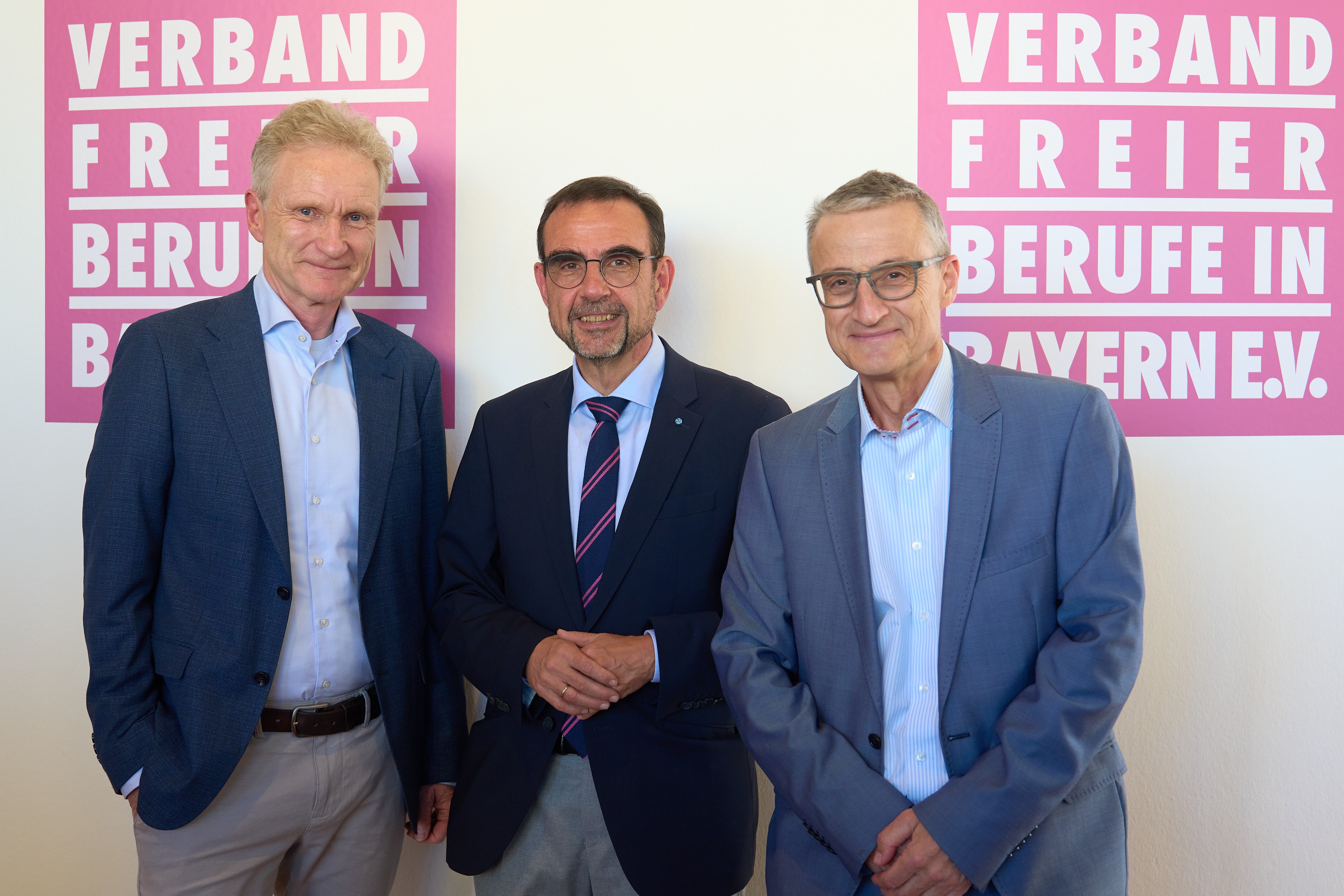 Drei Männer stehen nebeneinander. IM Hinetrrgund ist ein Plakat des Verbands Freier Berufe.